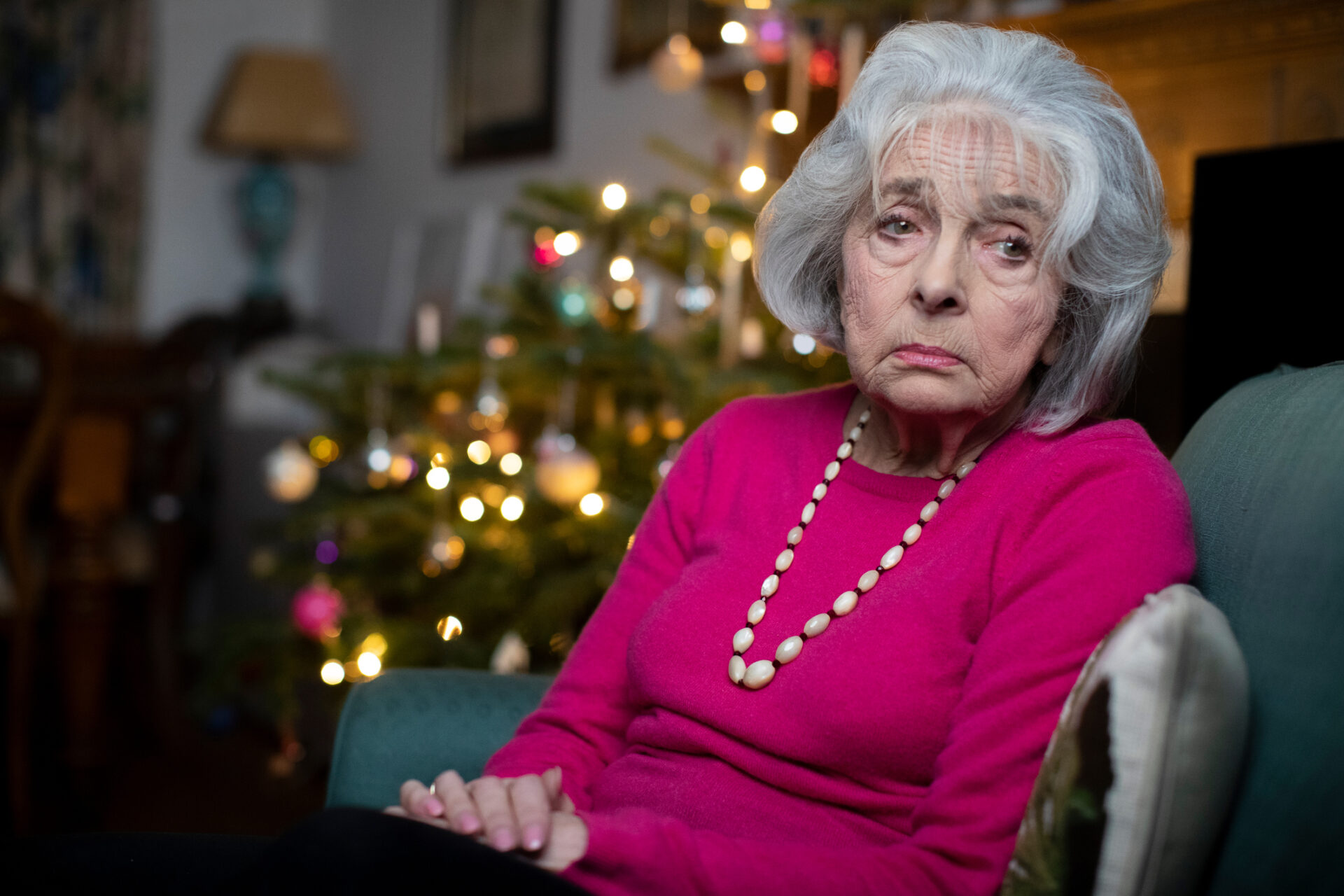 An older woman looking despondent with a Christmas tree behind her