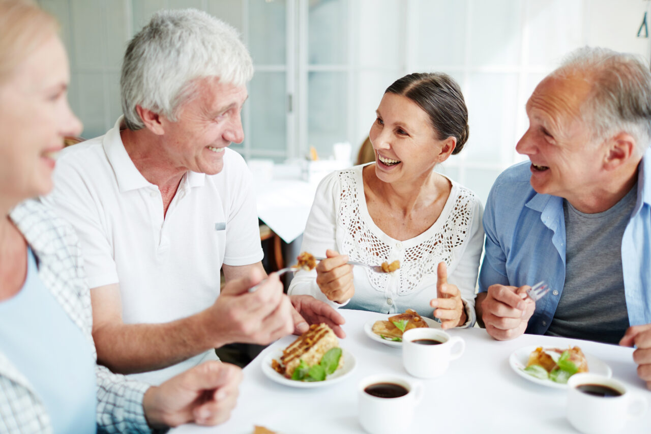Four older people sitting around a table laughing and eating