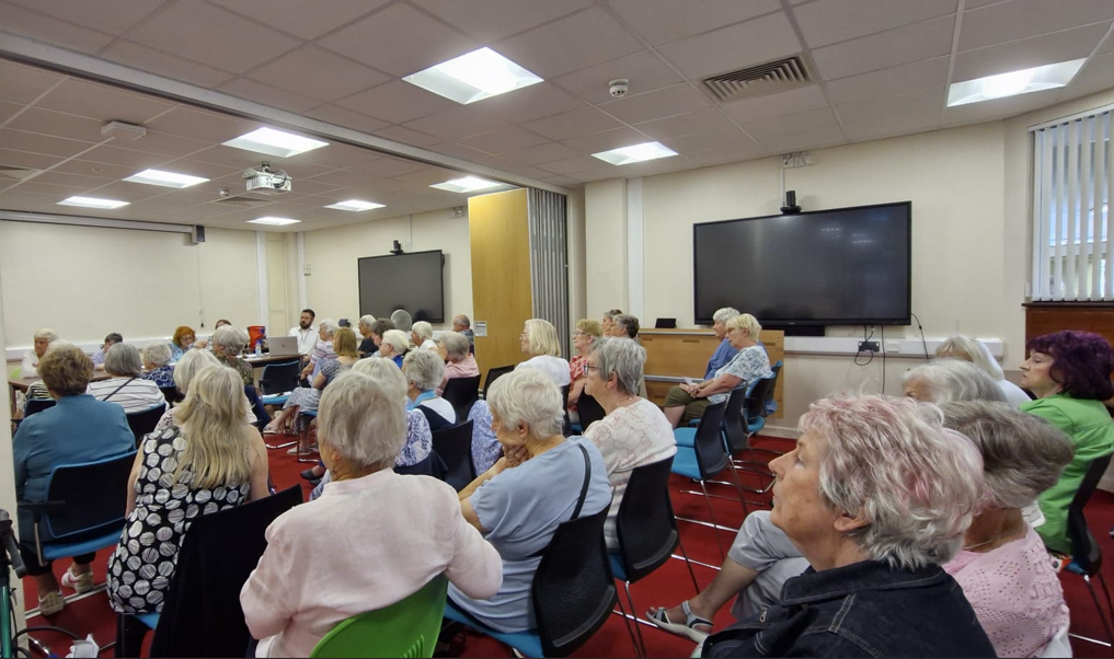 Delwedd o tua 60 o bobl hŷn, yn eistedd ar gadeiriau, yn mynychu cyfarfod ar y cyd o Fforymau 50+ Pont-y-pŵl, Cwmbrân a Blaenafon. Mae pawb yn eistedd yn wynebu siaradwr canolog.