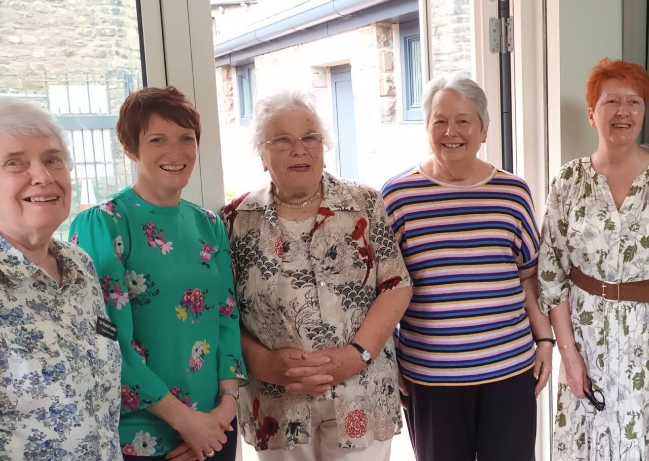 Rhian Bowen Davies, Comisiynydd Pobl Hŷn Cymru, yn y llun ochr yn ochr ag aelodau Fforwm 50+ Llandaf. Mae pawb yn y llun yn sefyll i fyny, y tu mewn i'r Pound, ger y fynedfa.