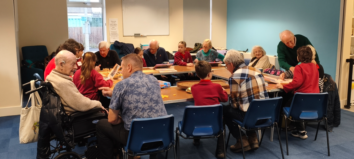Image of a group of older people, carers and family members sat around a table at the Dementia Supportive group in Saundersfoot.
