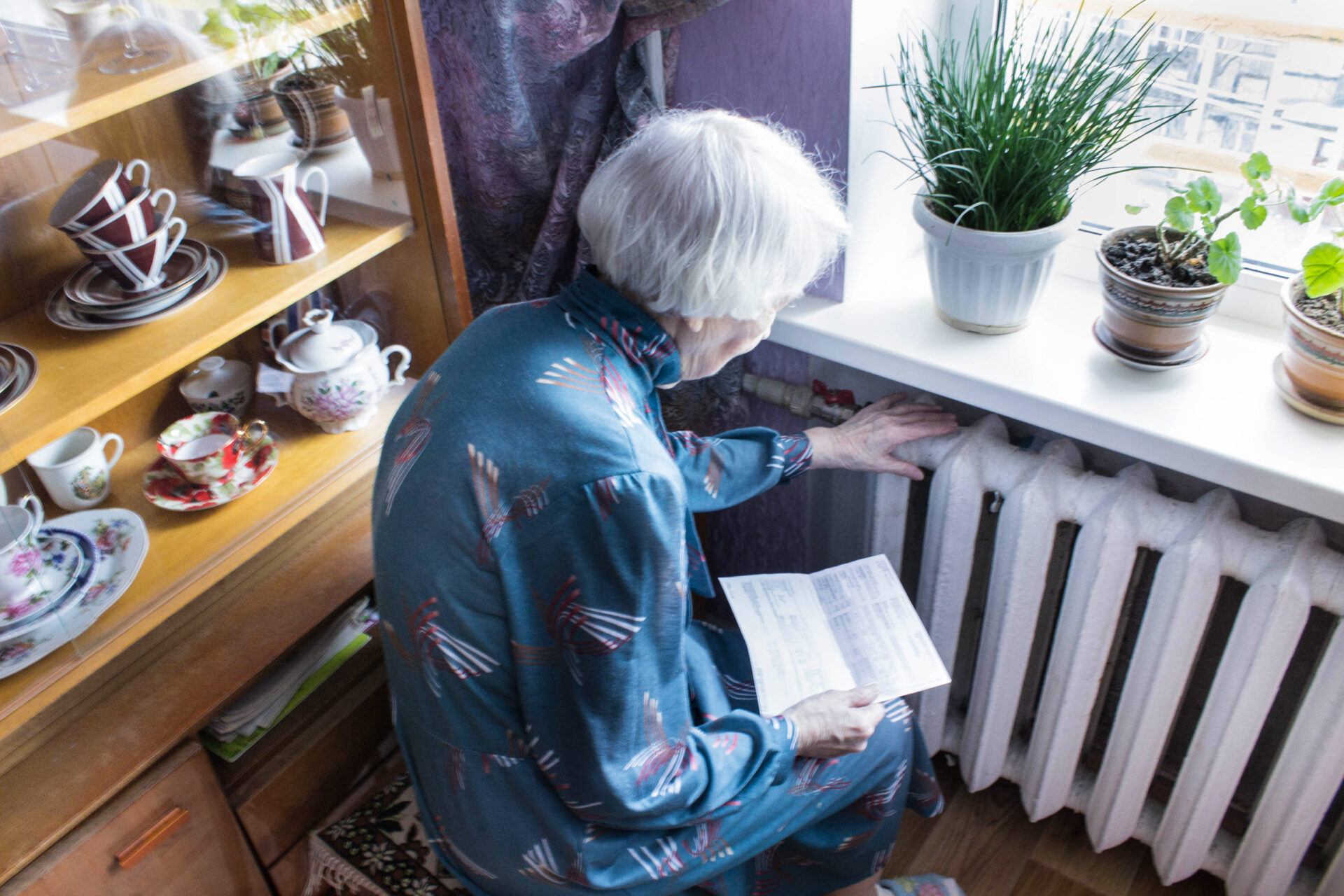 Older woman holding gas bill in front of heating radiator.