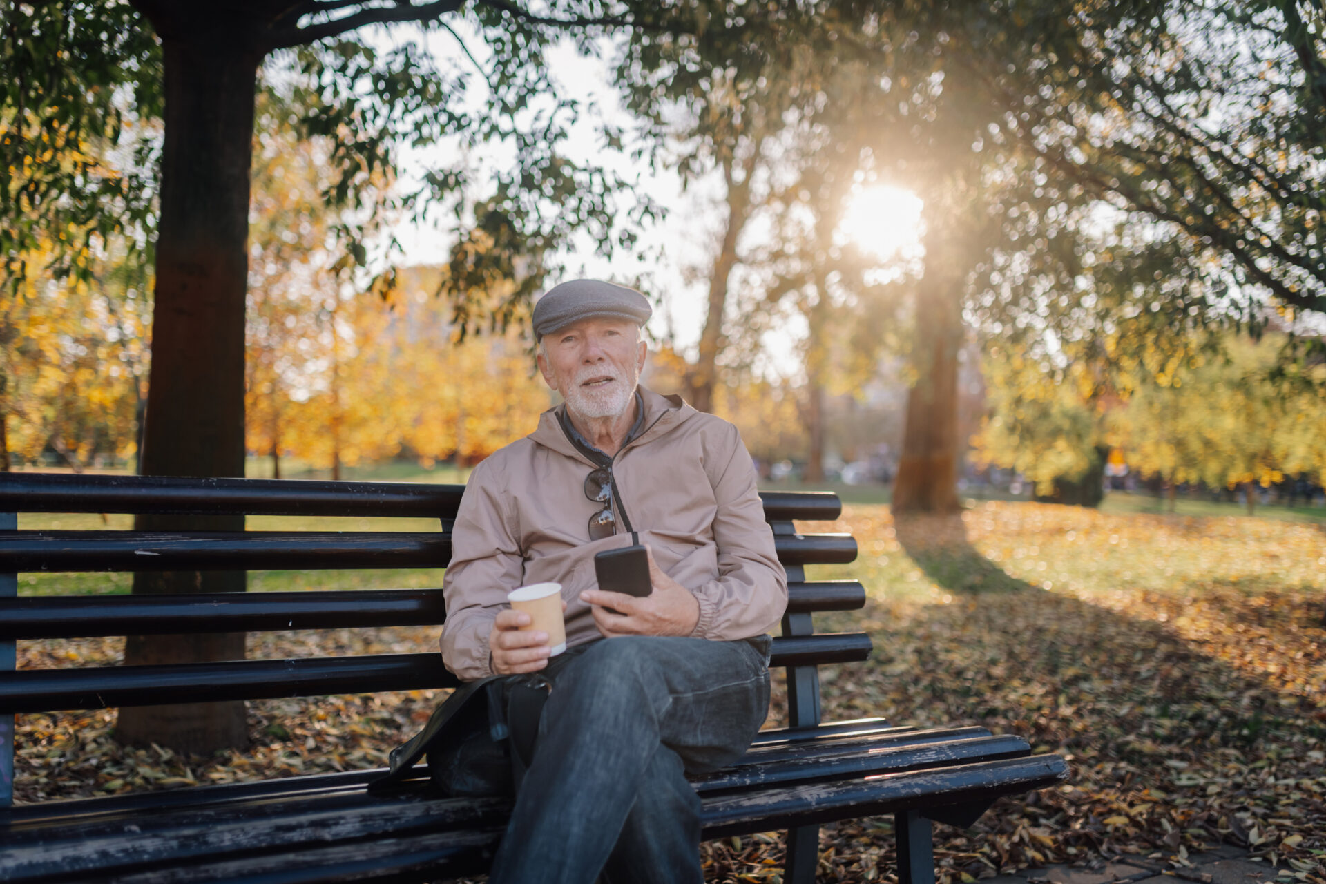 Delwedd o ddyn hŷn yn eistedd ar fainc parc ar noson heulog. / Image of an older man sat on a park bench on a sunny evening.