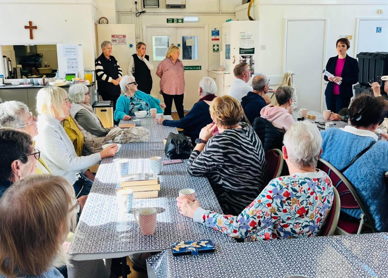 Safodd Comisiynydd Pobl Hŷn Cymru, Rhian Bowen-Davies (ar y dde ar y brig), yn Eglwys Sant Pedr yn Aberbargoed, gan siarad ag aelodau o Grŵp Hen Gyfeillion Aberbargoed. // Older People’s Commissioner for Wales, Rhian Bowen-Davies (top-right), stood in St Peter’s Church in Aberbargoed, speaking to members of the Aberbargoed Old Friends Group.